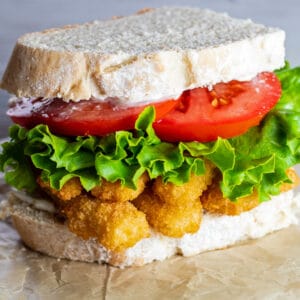 Fish stick sandwich with lettuce and tomato, on a plain background.