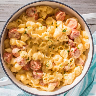 Mac and cheese with hot dogs in white pot on wooden background.