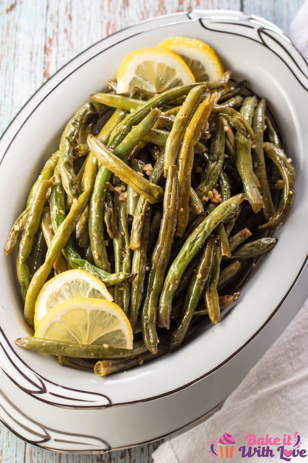 Tall image of the roasted green beans in white serving bowl with lemon.