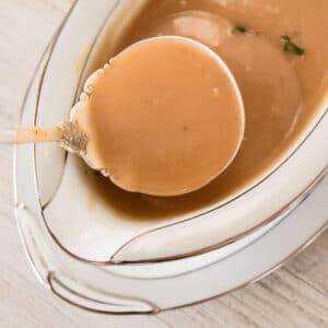 Turkey gravy being ladled out of a white dish.