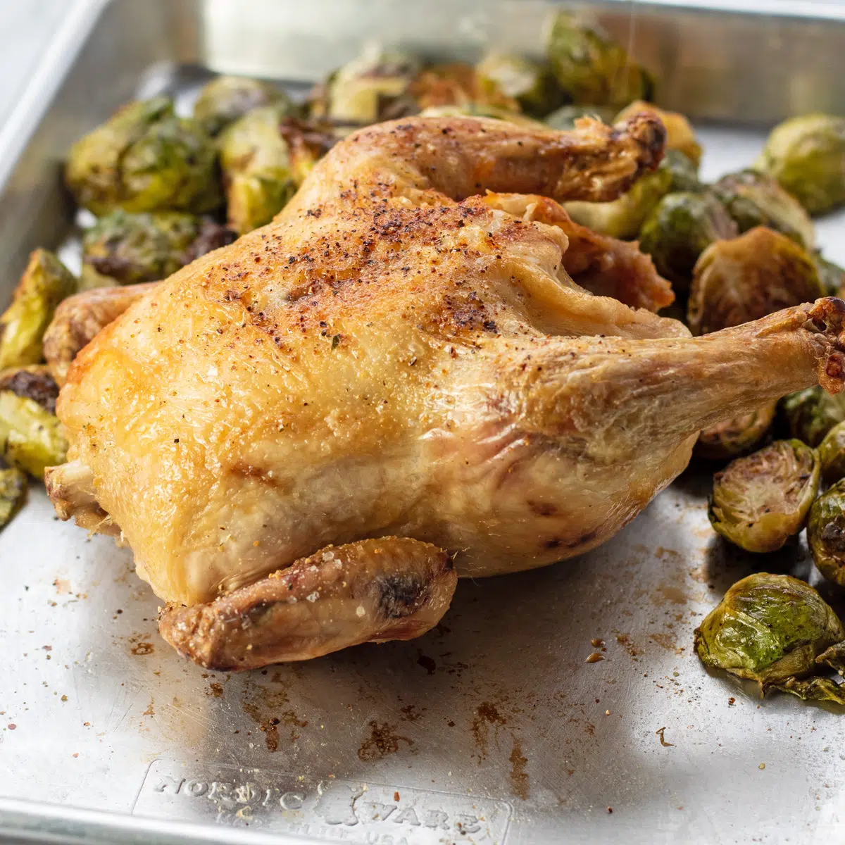 Air fryer Cornish hen on baking tray with roasted brussel sprouts.