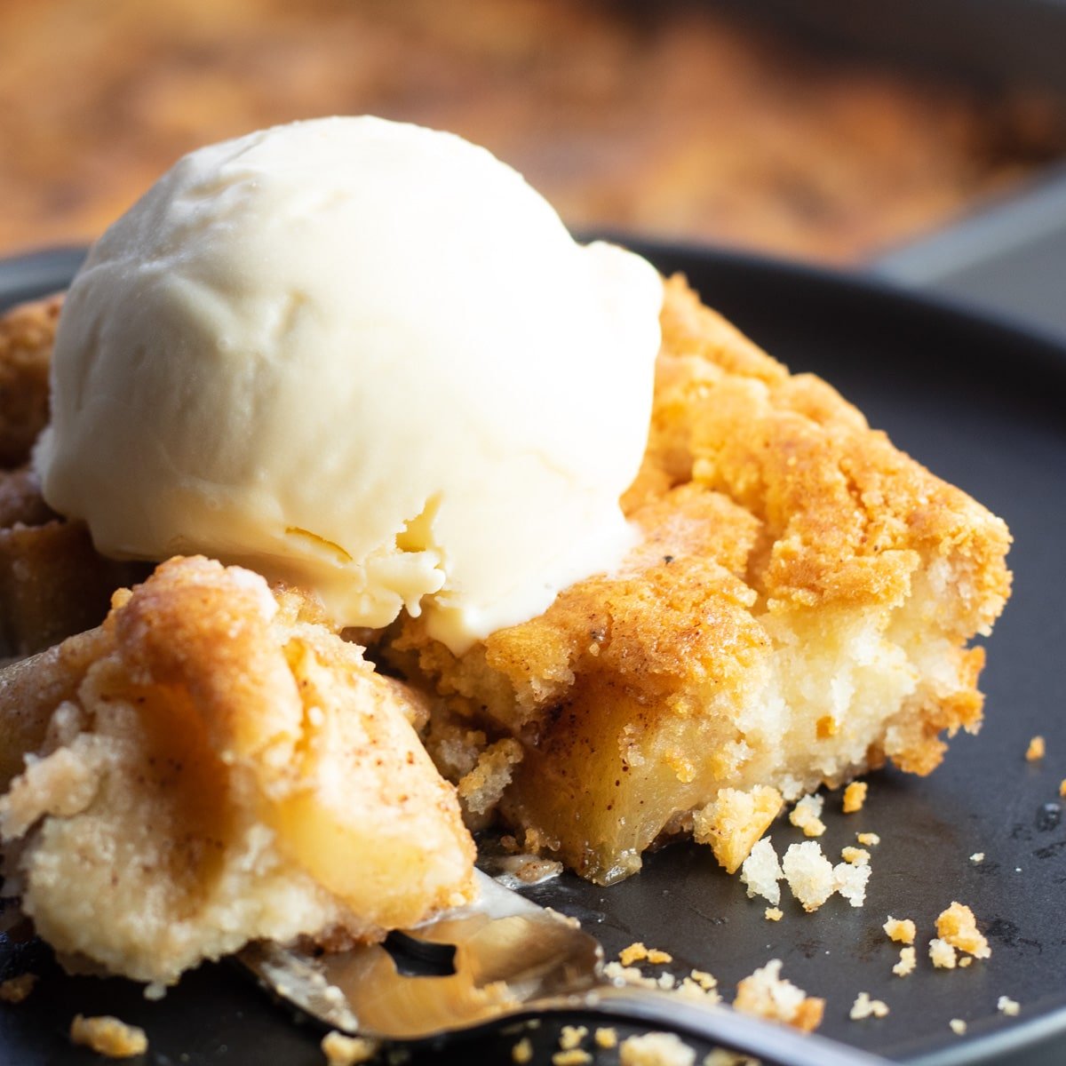 Bisquick apple cobbler disajikan di piring hitam dengan porsi di atas garpu.