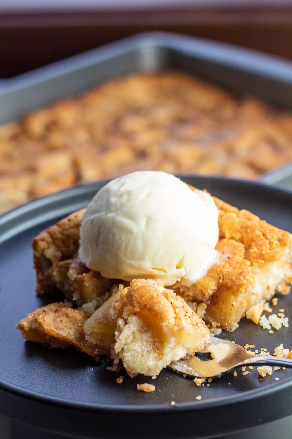 Bisquick apple cobbler on black plate with pan in background.