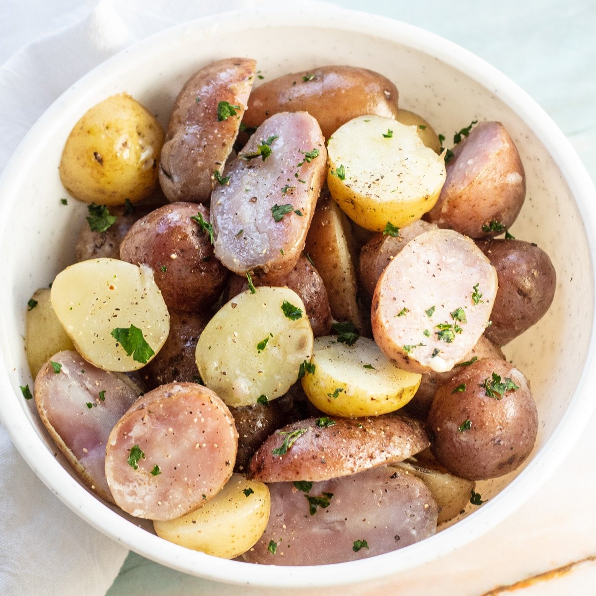 Batatas cozidas em uma tigela branca com salsa por cima.