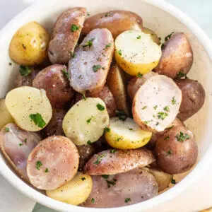 Boiled potatoes in a white bowl with parsley on top.