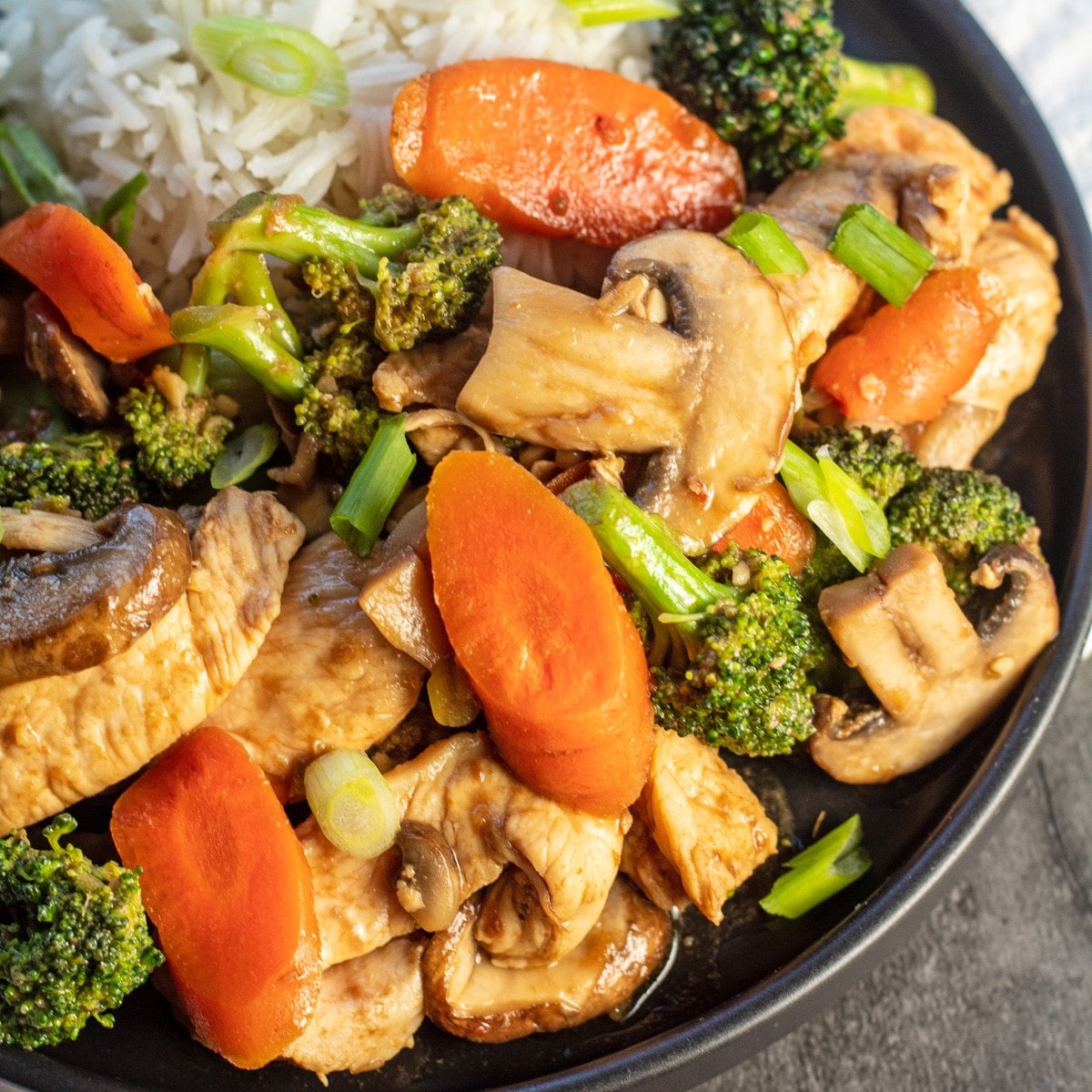 Chicken with garlic sauce served with rice on black plate.