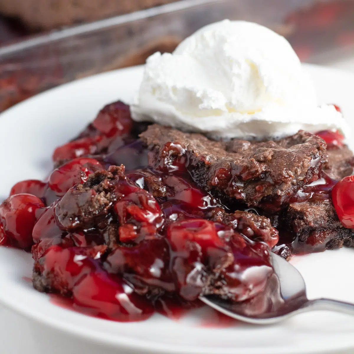 Chocolate cherry dump cake served with whipped cream on top and a spoonful in front.