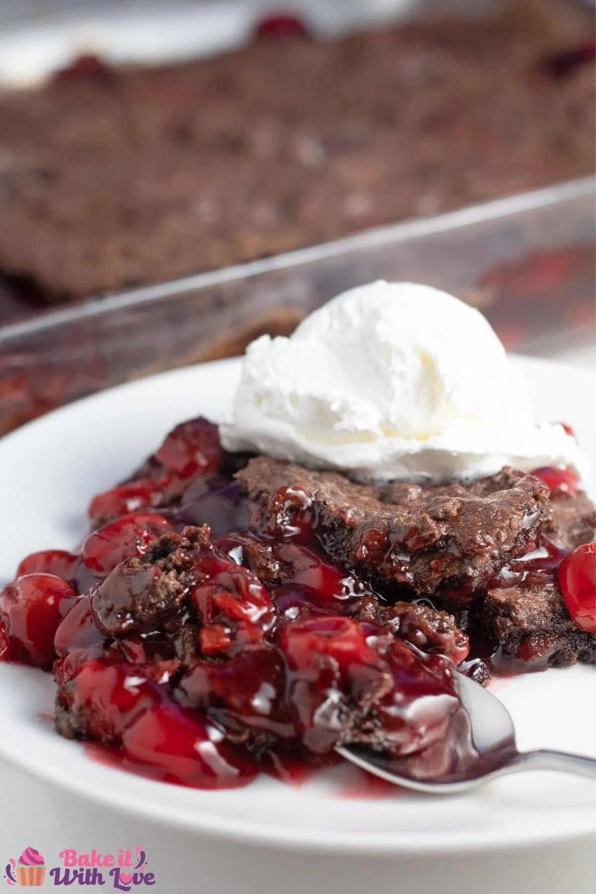 Tall image of the chocolate cherry dump cake served on plate with the baking dish in background.