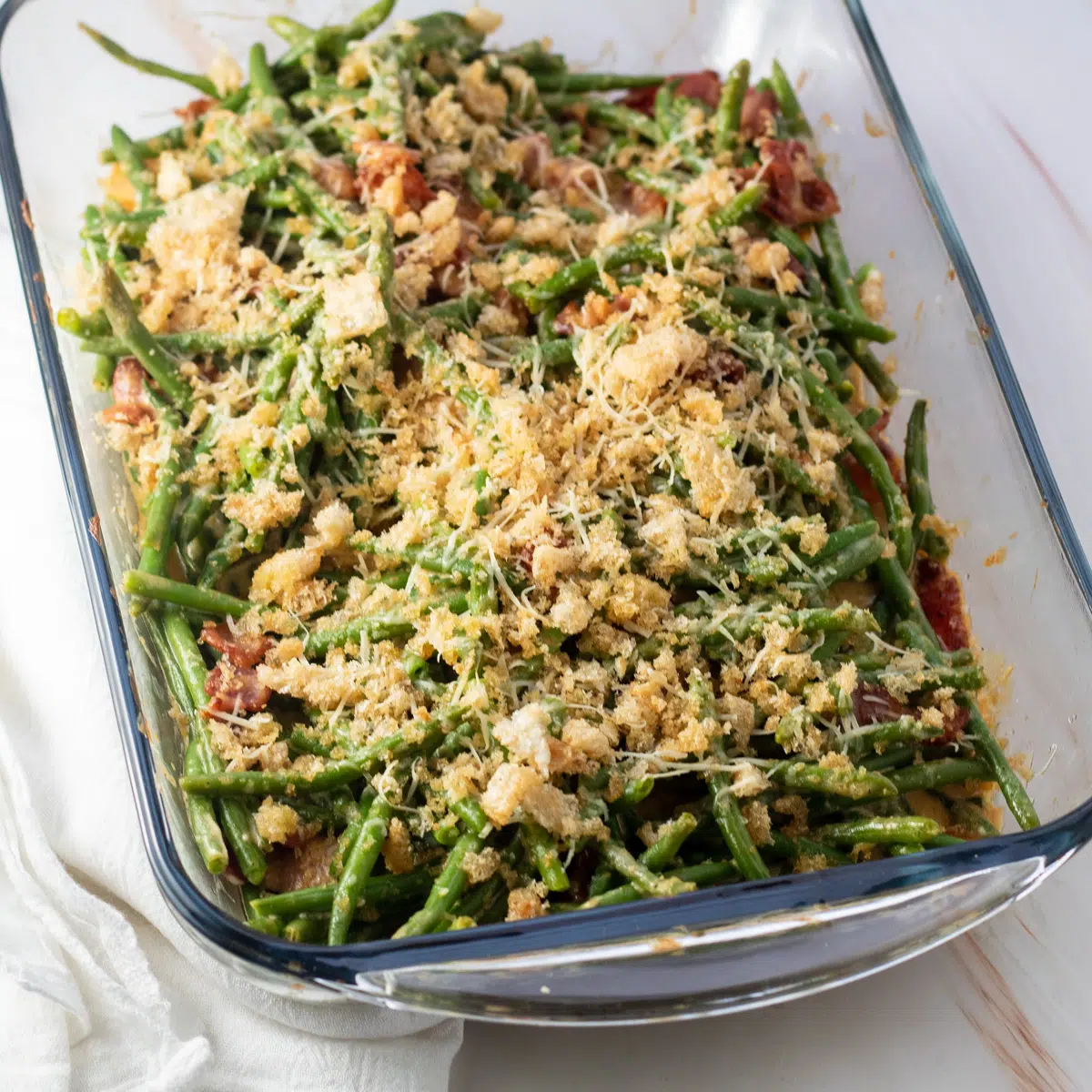 Green bean casserole with bacon in glass baking dish on light background.