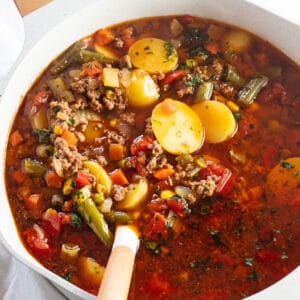 Hearty hamburger soup in stock pot with ladle.