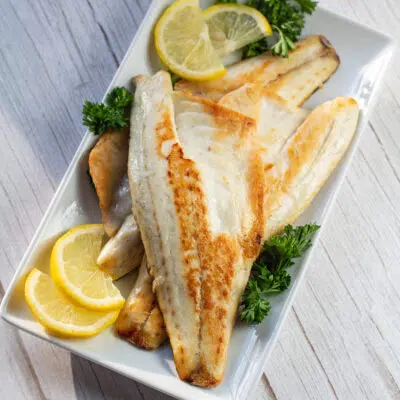 Pan seared sea bass fillets on platter with parsley and lemon.
