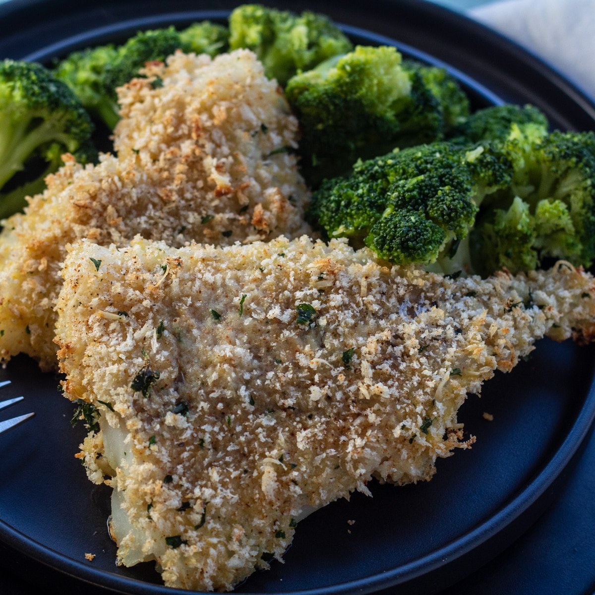 Panko baked cod served with broccoli on black plate.