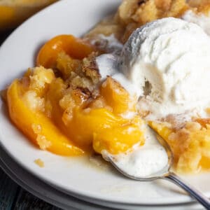 Peach dump cake on white plate with whipped cream.