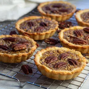 Pecan tartlets on cooling rack with scattered pecans.