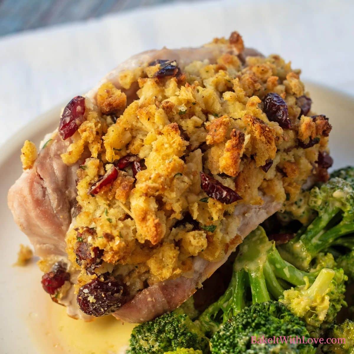 Square image of stuffing stuffed pork chops on a white plate with a side of broccoli.