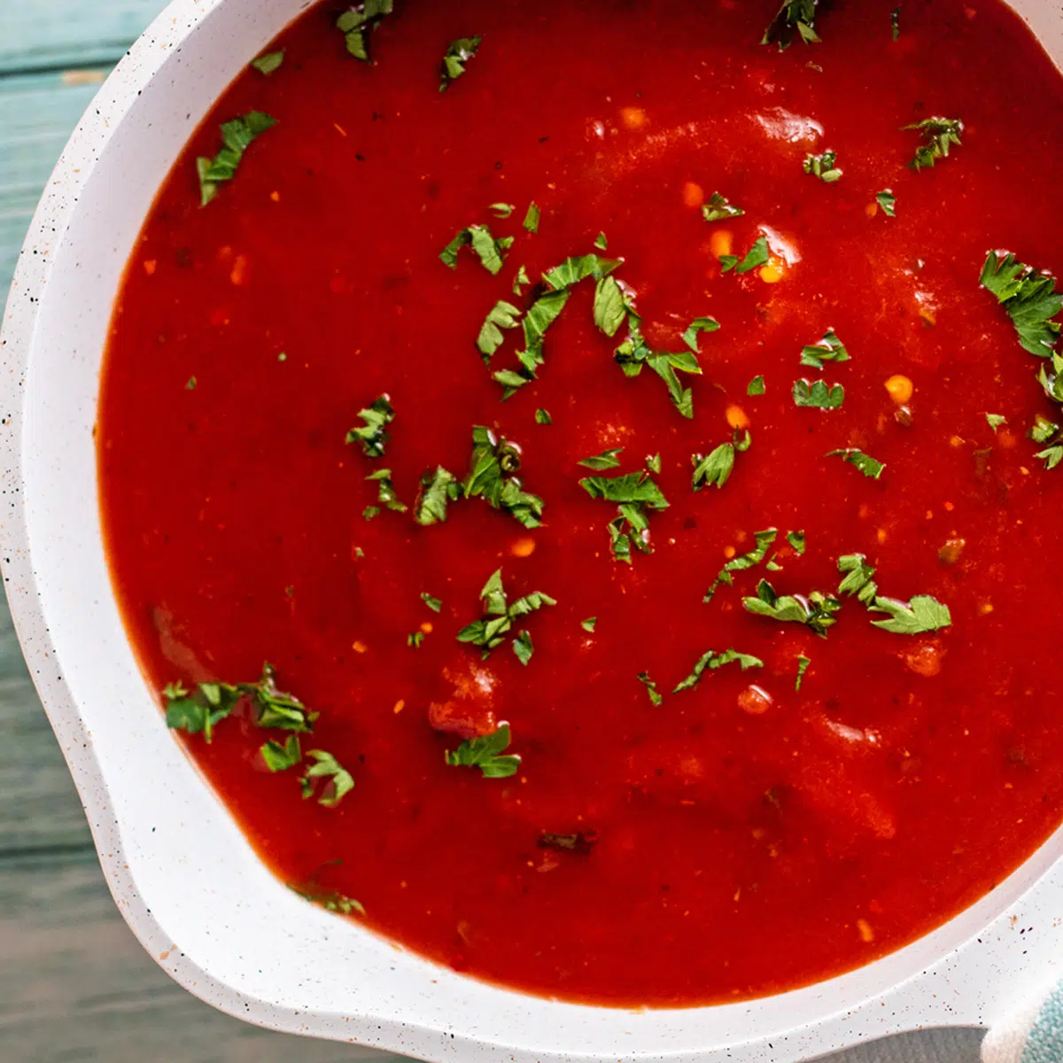 Molho de arrabbiata em panela de cor clara com guarnição de salsa.