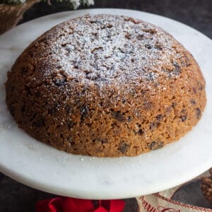 Christmas pudding dusted with confectioners' sugar served on marble cake stand.
