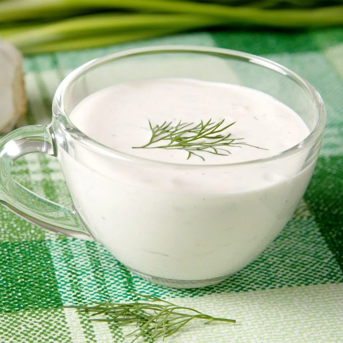 Sustituto de la crema fresca para cocinar y hornear, presentado en un vaso transparente con eneldo fresco.