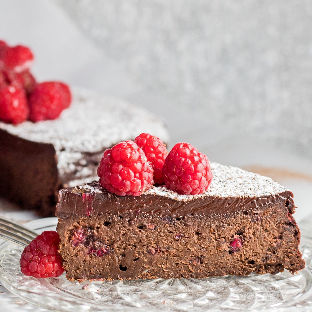 Kue raspberry coklat tanpa tepung yang diiris dengan raspberry di atasnya.