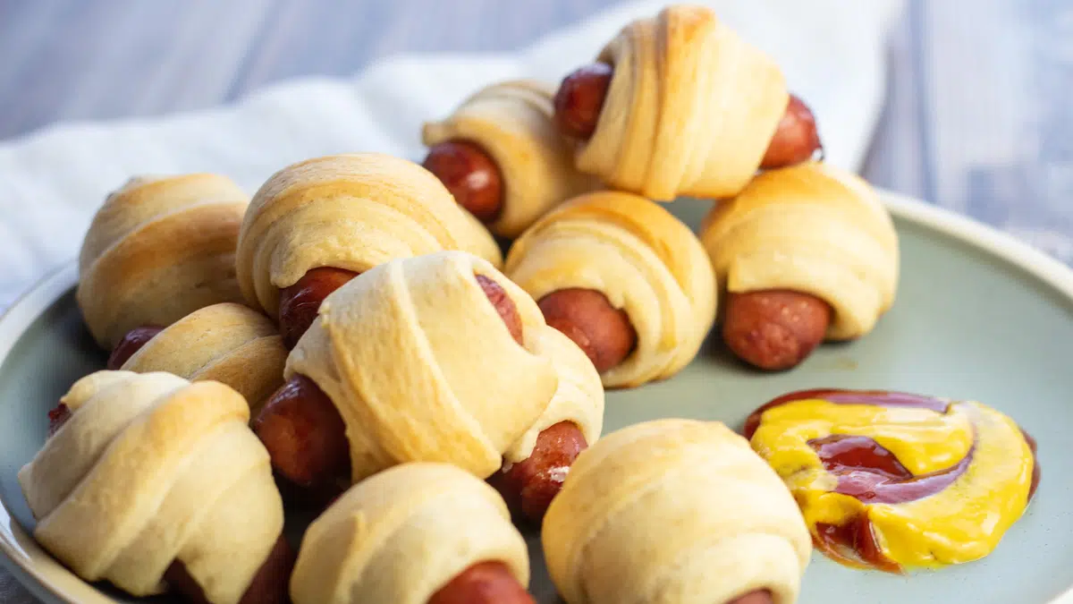 Wide image of the lil smokies pigs in a blanket served on sage green plate.