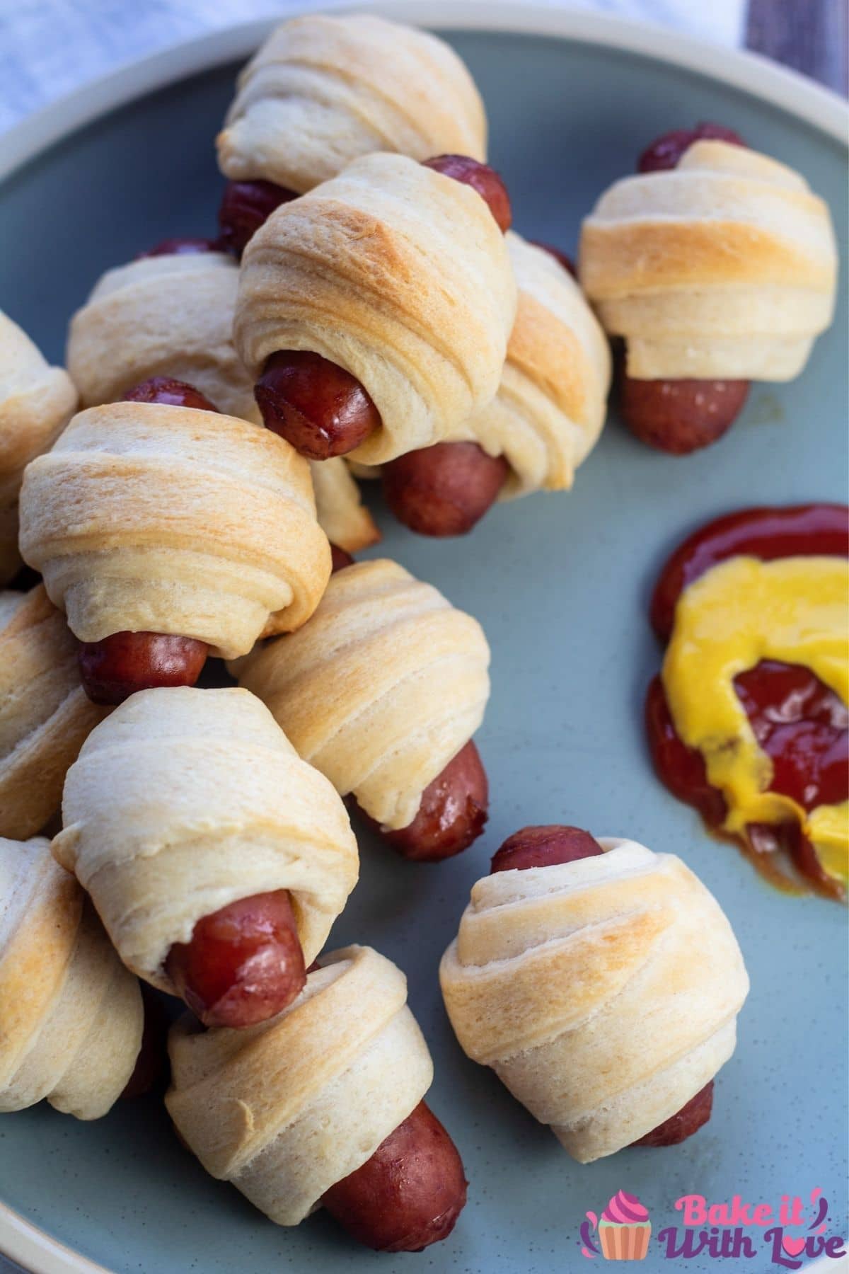 Tall image of the lil smokies pigs in a blanket on plate with condiments.