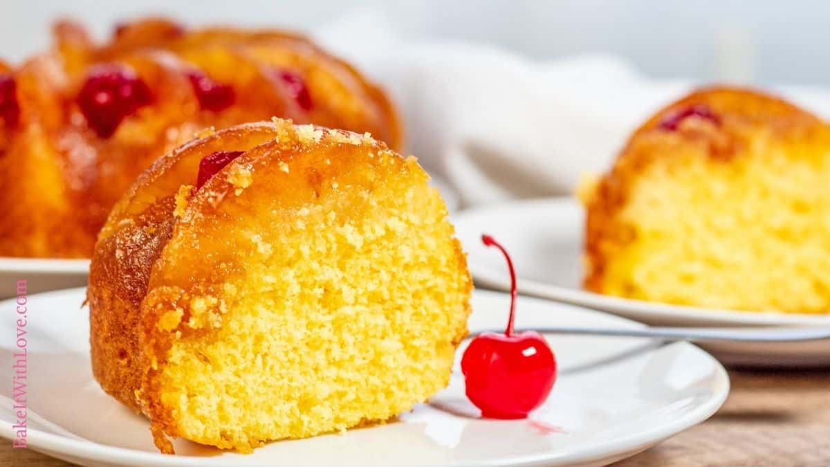 Pineapple upside down bundt cake slice on a white plate with more slices in background and a cherry next to the slice.