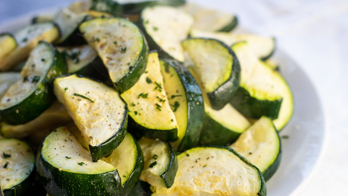 Air fryer zucchini on white plate with black pepper and parsley.