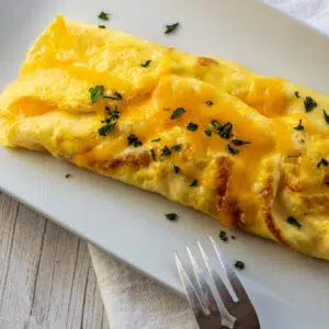 Delicious cheese omelet on white plate with fork set next to it.