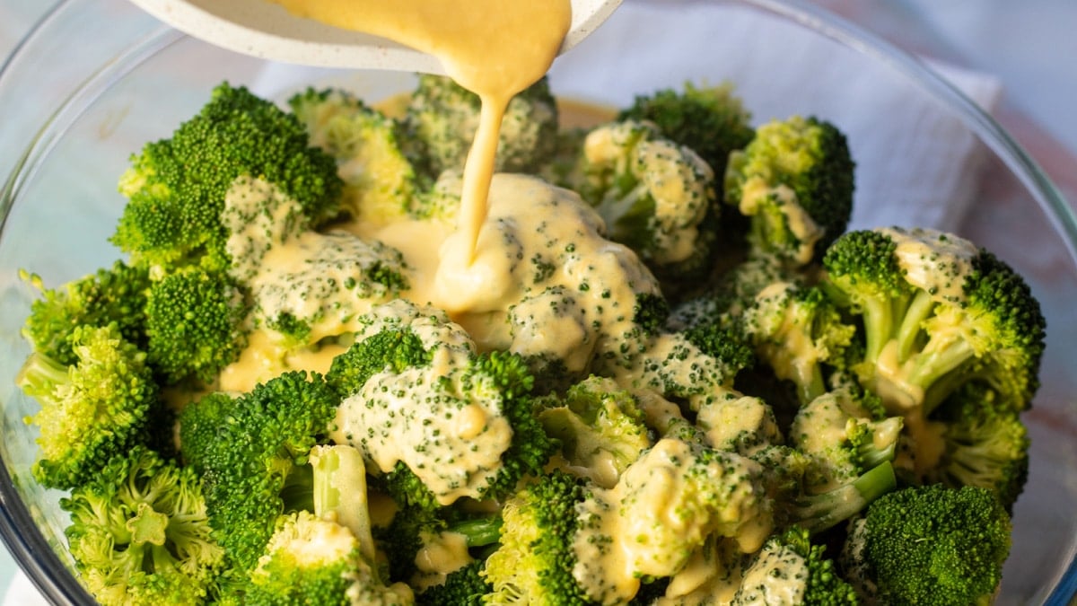 Široký obraz sýrové omáčky na brokolici, která se nalévá.