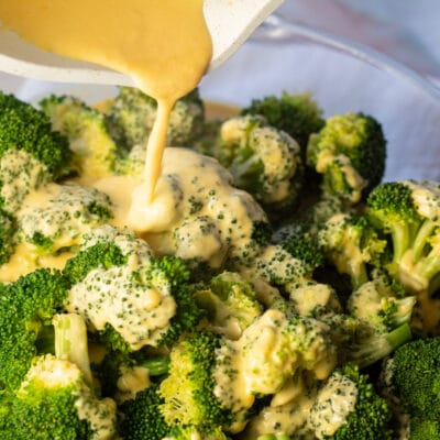 Closeup on the cheese sauce for broccoli being poured over veggies.
