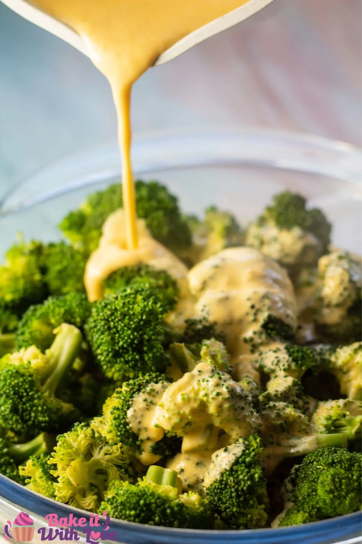 Tall image of pouring the cheese sauce for broccoli into a bowl of steamed broccoli.