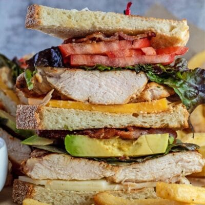 Chicken club sandwich with fries on a parchment.