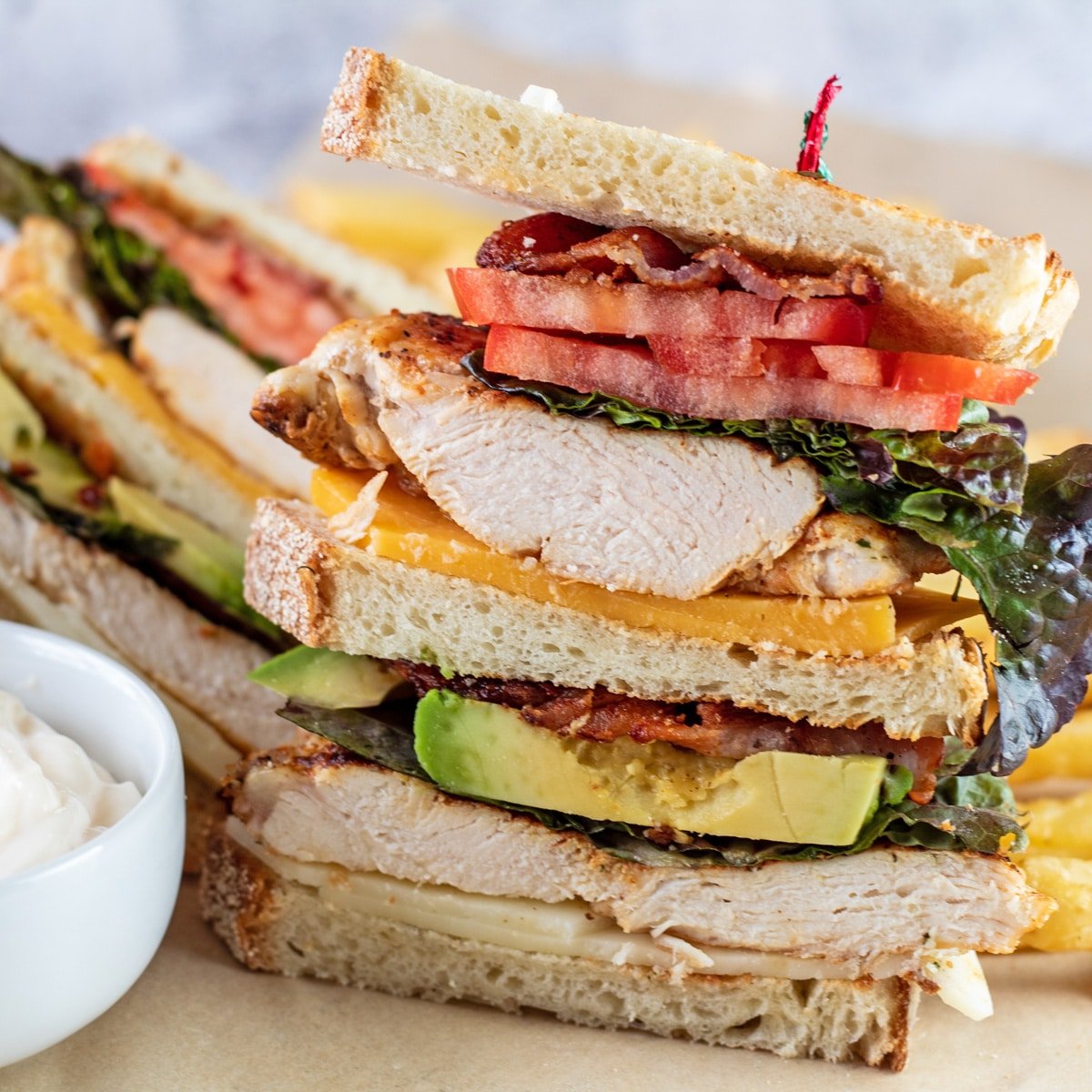 Chicken club sandwich with fries on a parchment.