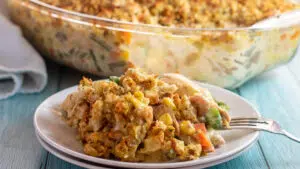 Wide image of the plated chicken stuffing casserole with glass baking dish in background.