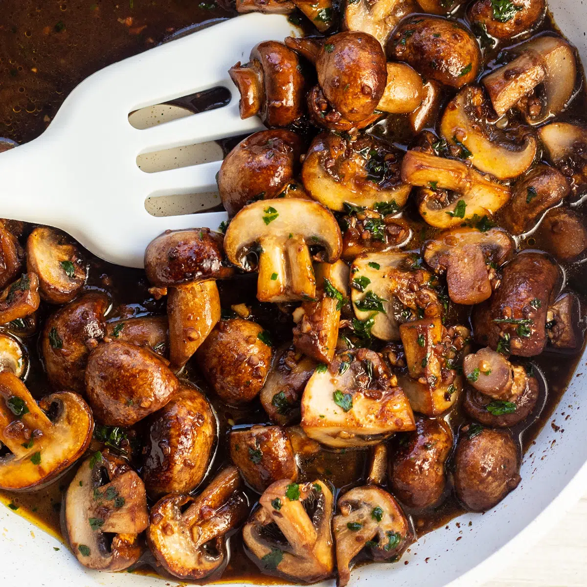 Knoflookboter champignons in koekenpan met witte spatel.