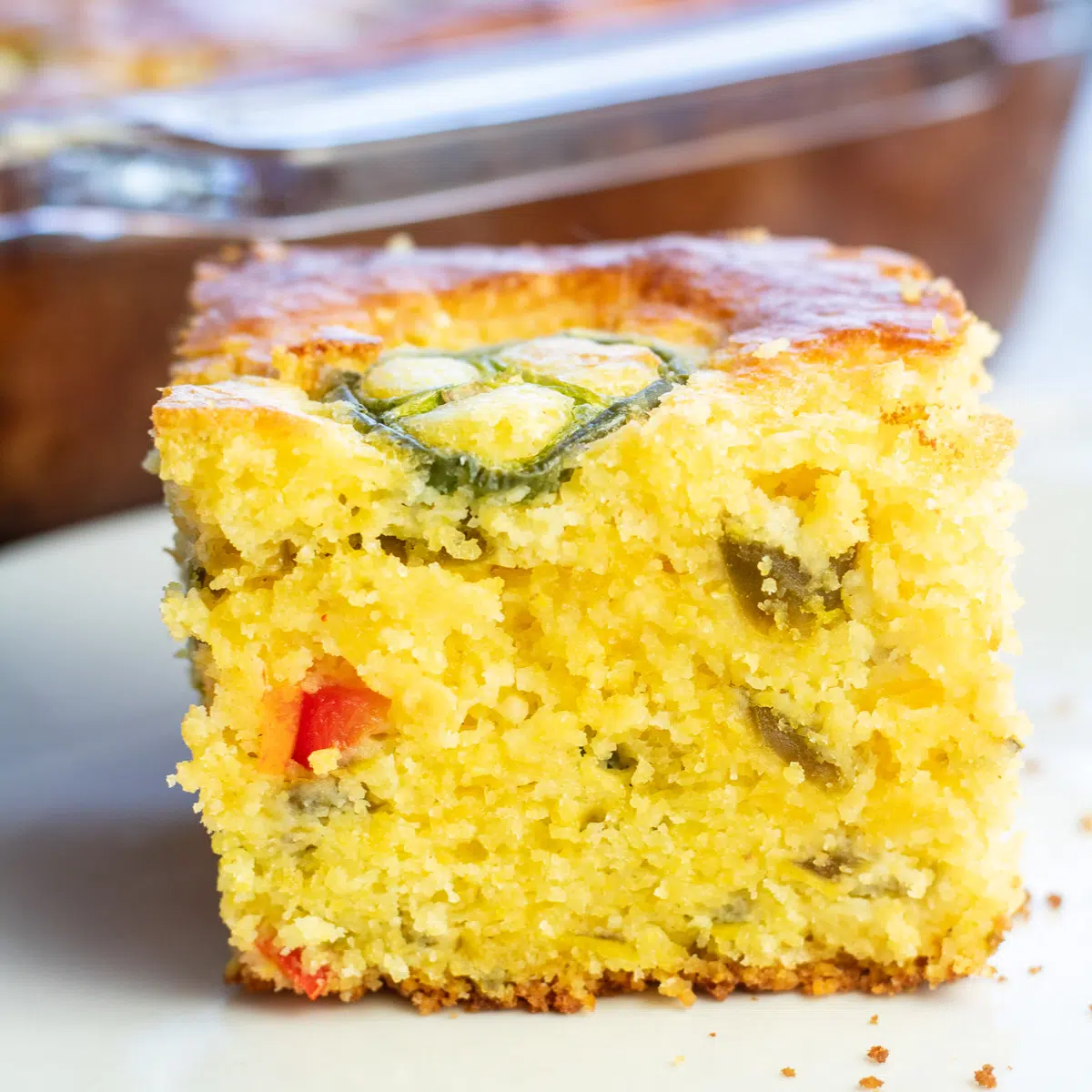 Jiffy jalapeno cornbread served on white plate with baking dish in background.