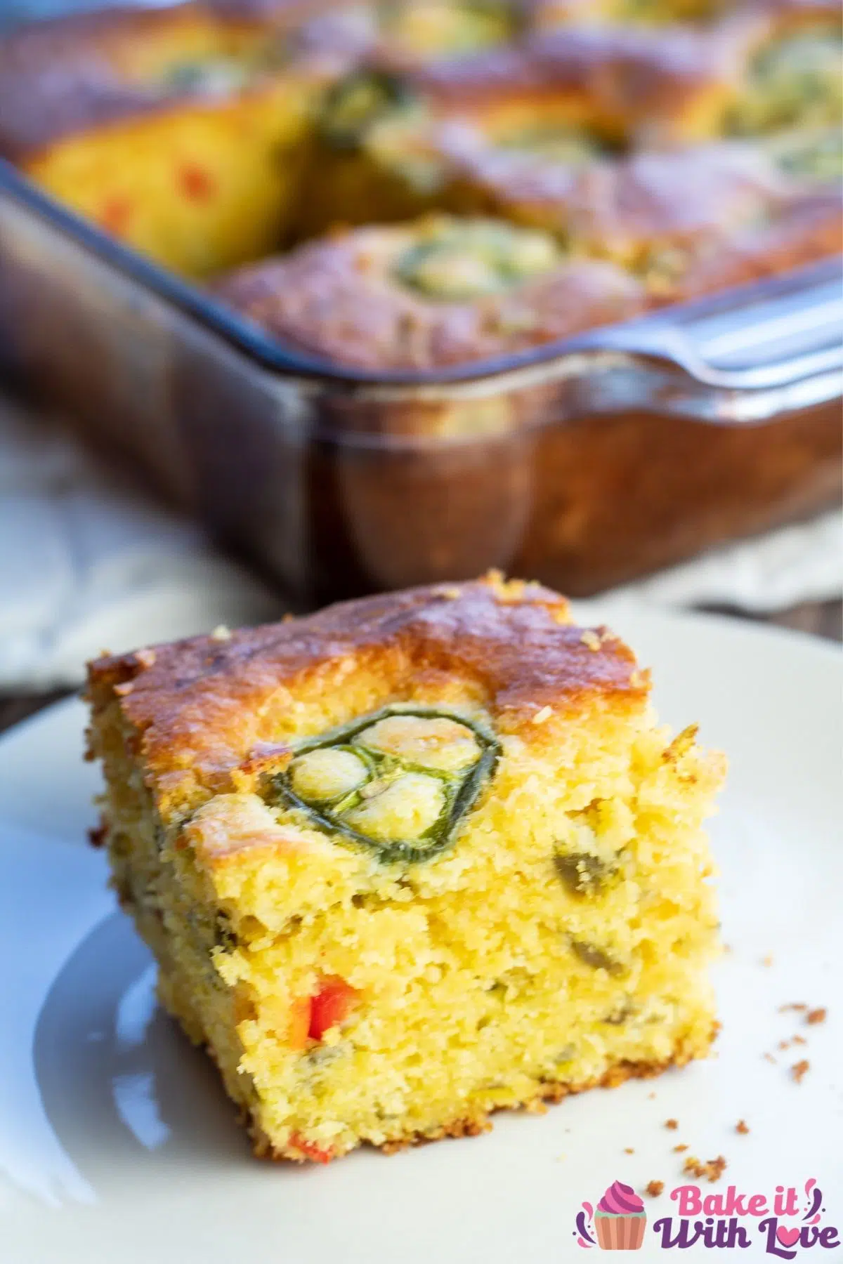 Tall image of a single sliced jiffy jalapeno cornbread square and pan in background.