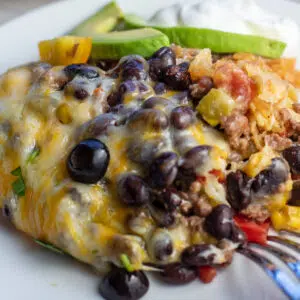 Closeup on the Mexican ground beef casserole plated on white dish topped with sour cream and avocado.