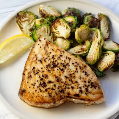 Pan seared swordfish plated with lemon wedge and brussel sprouts.