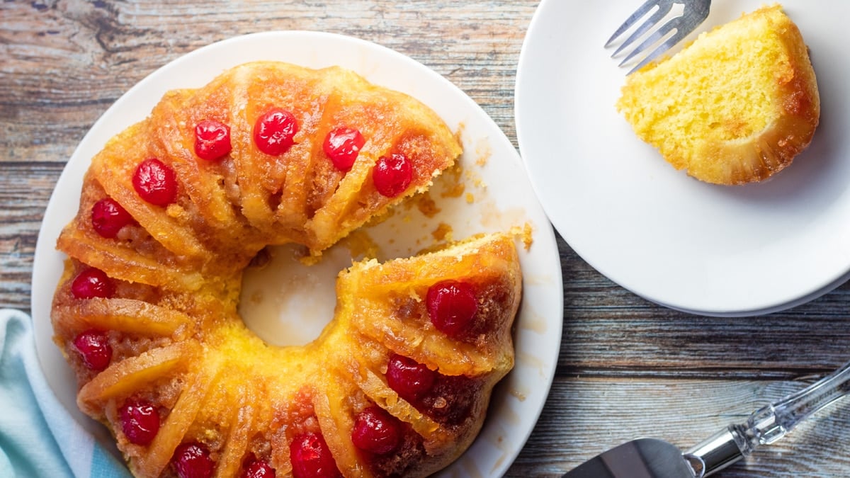 Wide overhead image of the pineapple upside down bundt cake with a slice on white plate.