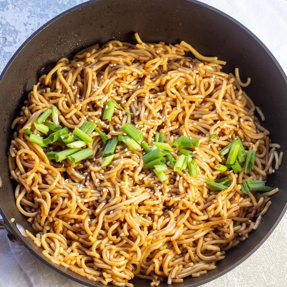 Teriyaki noodles served in skillet with sesame seed and green onion garnish.
