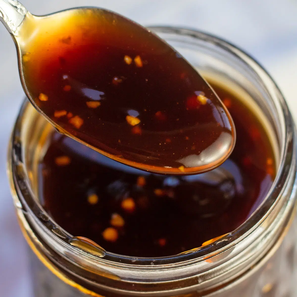 Tangy, thickened teriyaki sauce being spooned from glass jar.