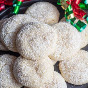 Biscotti crinkle alla vaniglia spolverati di zucchero dei confettieri con nastri natalizi sullo sfondo.