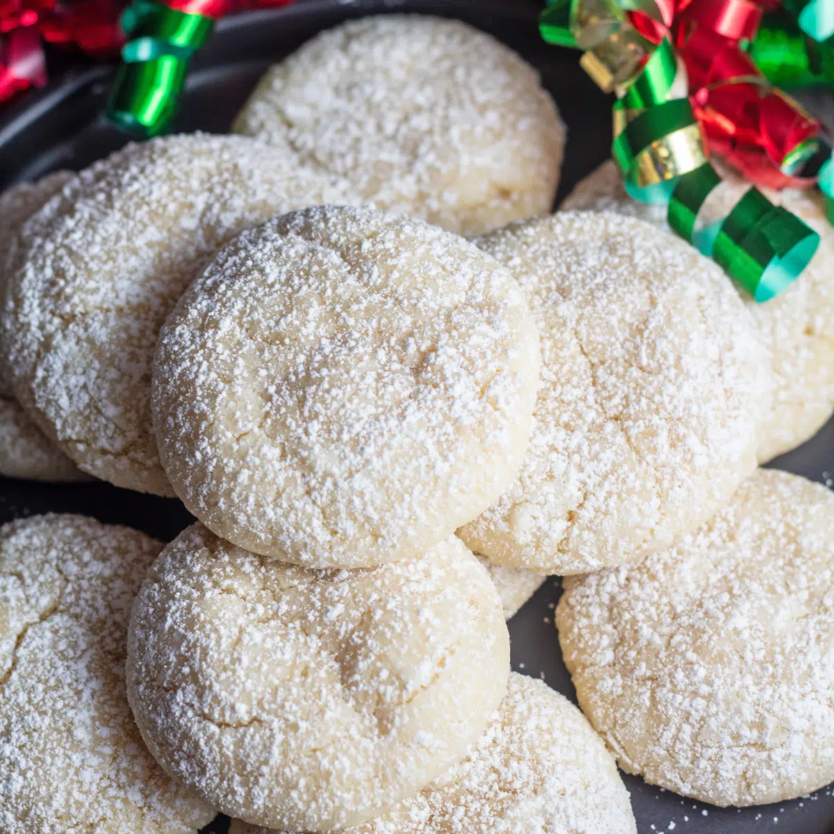 Konditoren suagr bestäubte Vanille-Crinkle-Kekse mit Feiertagsbändern im Hintergrund.