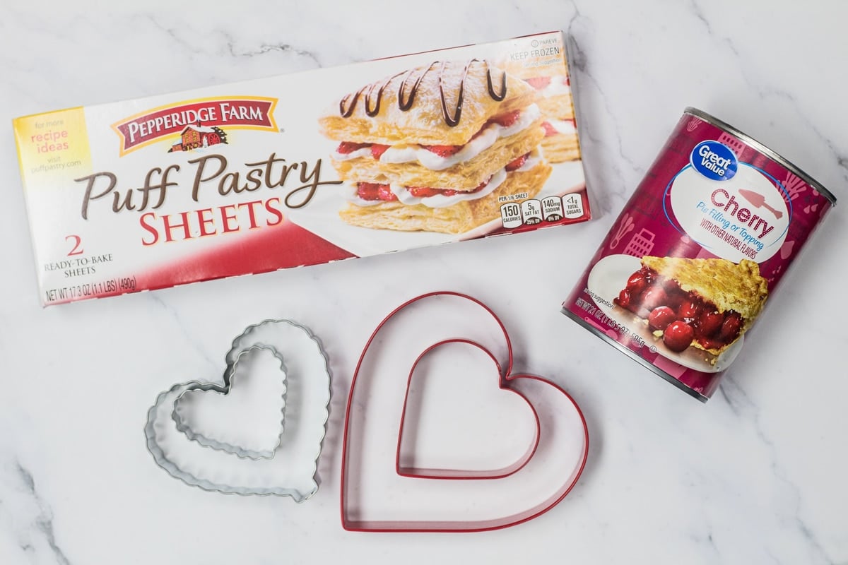 Puff pastry hearts ingredients with puff pastry sheets, cherry pie filling, and heart cookie cutters.