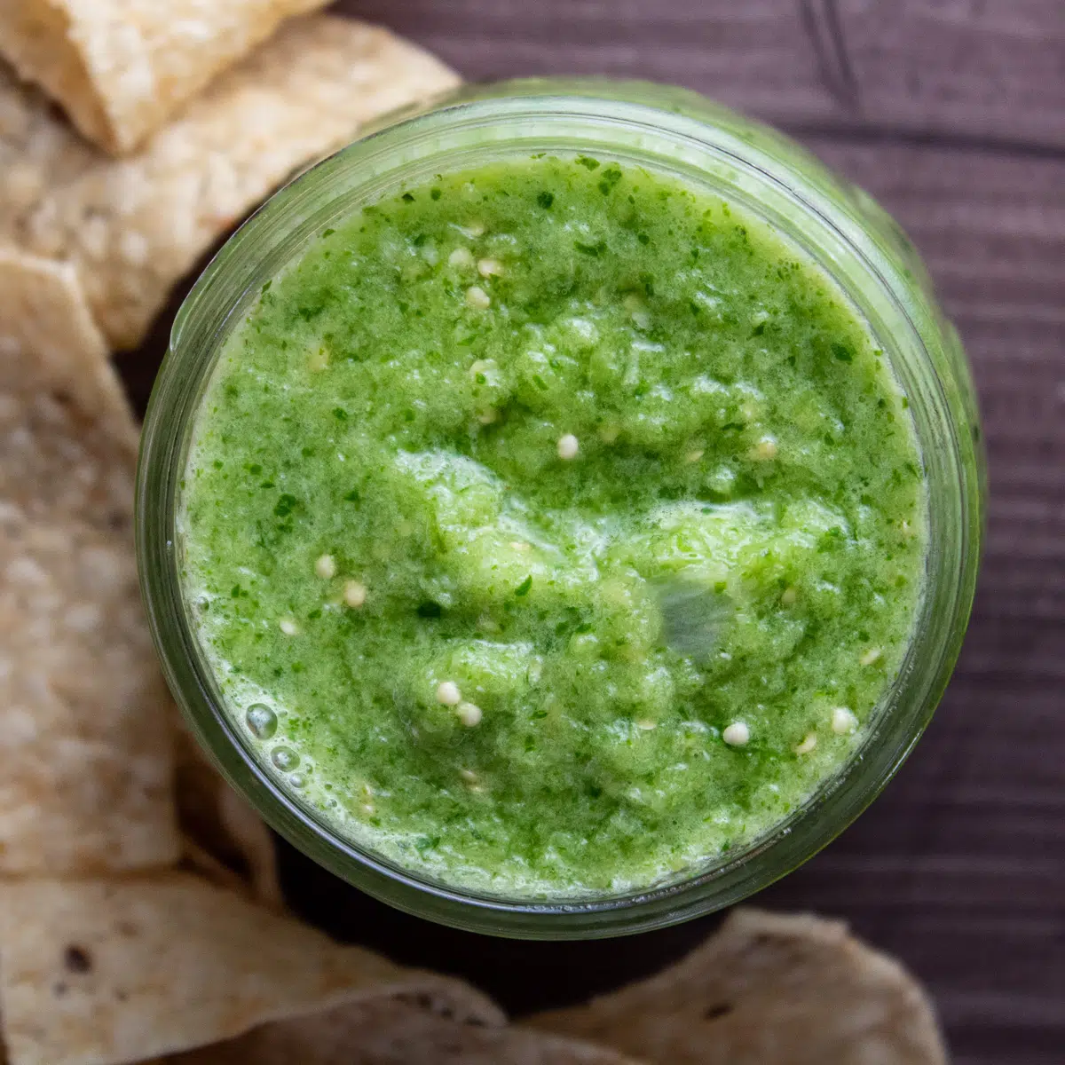 Square overhead image of salsa verde in a jar with tortilla chips.