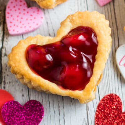 Puff pastry hearts with cherry pie filling on wooden grain background.