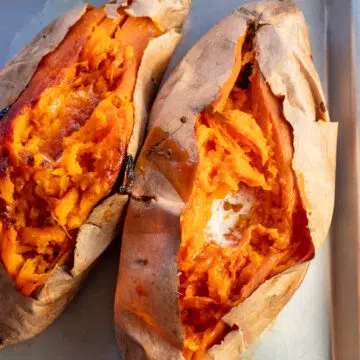 Baked sweet potatoes on a metal tray opened with a pat of butter inside.