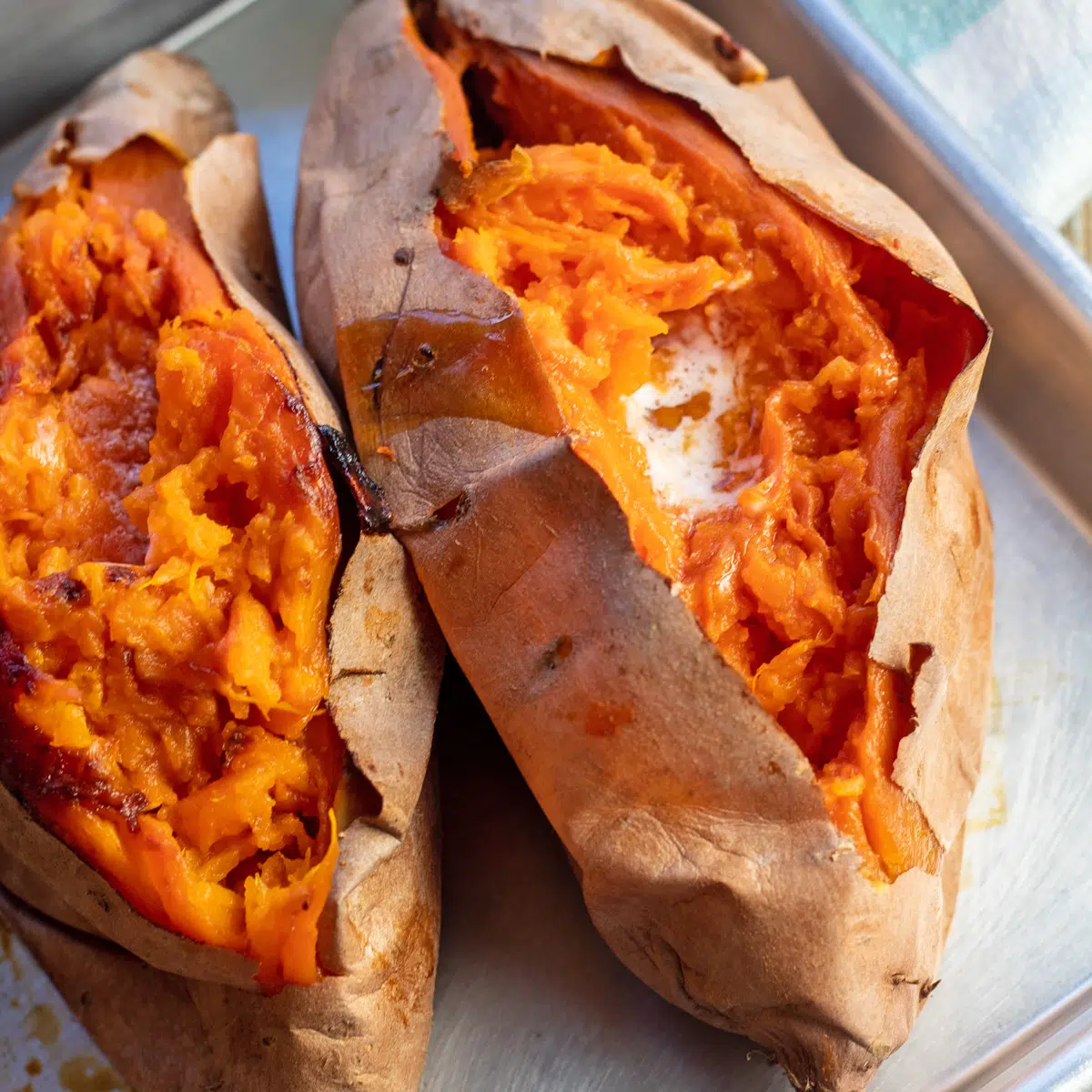 Baked sweet potatoes on a metal tray opened with a pat of butter inside.