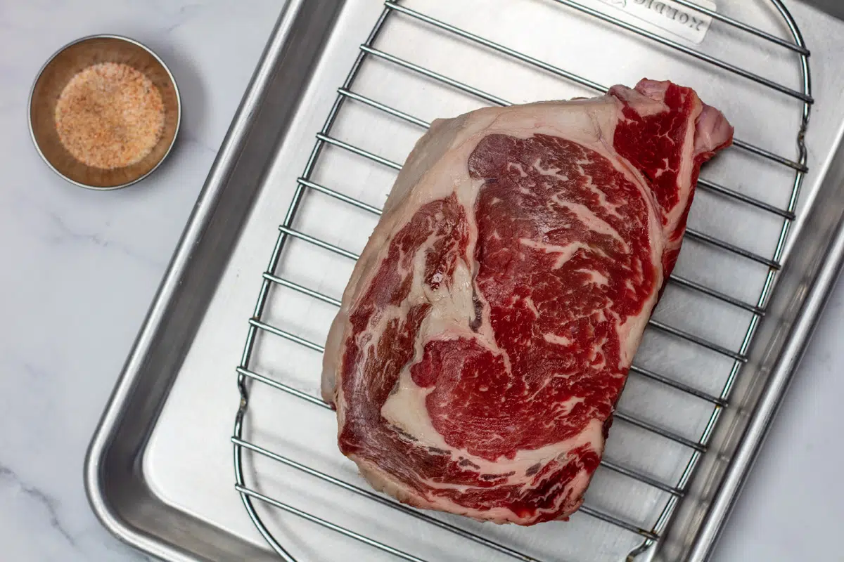 Ingredient photo showing a ribeye steak and seasoning in a broiler pan.